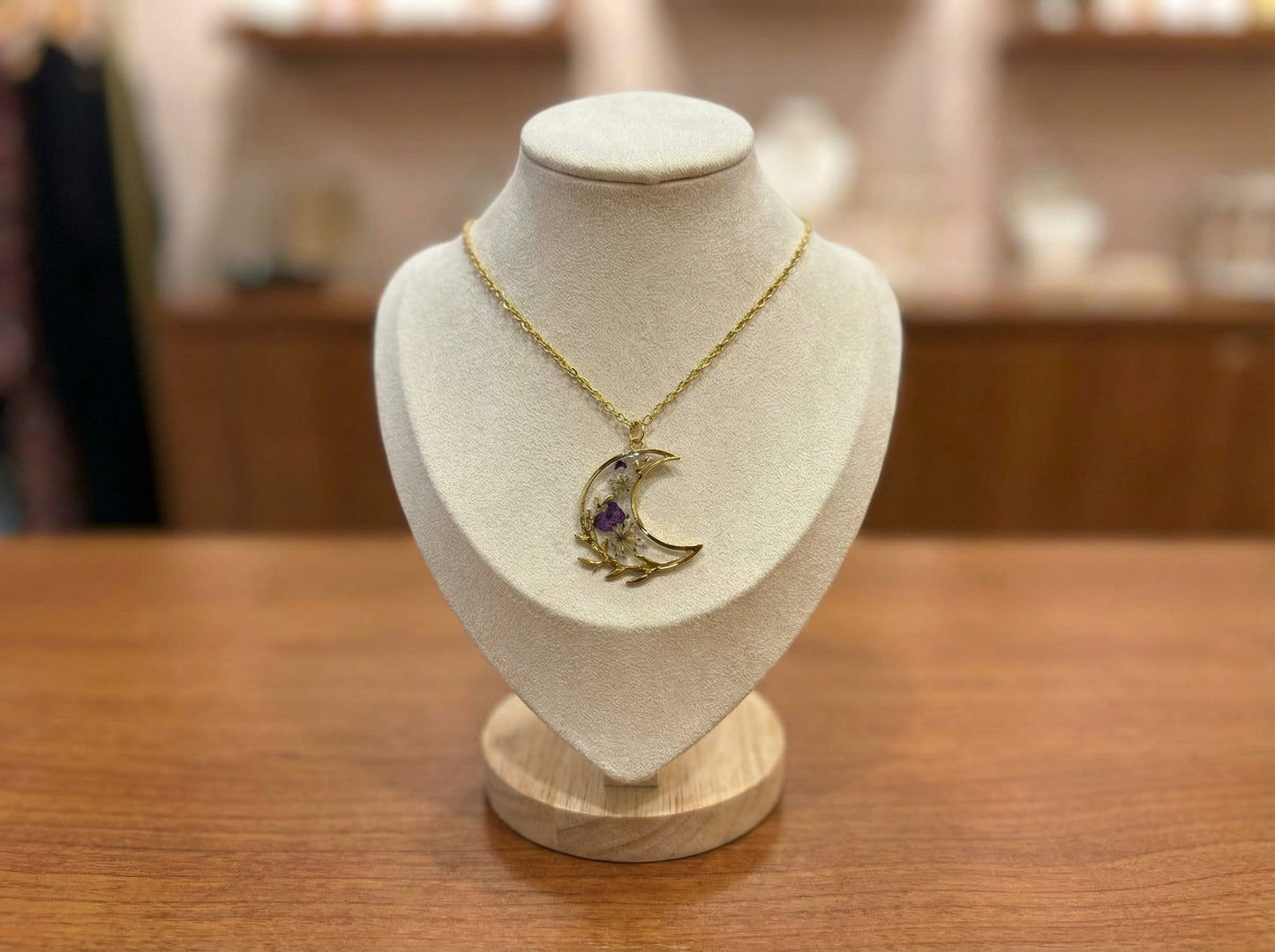 Collier Lune Botanique Améthyste de Les Lubies Fleuries, mettant en valeur des fleurs séchées violettes sous un pendentif en croissant de lune dans une monture dorée raffinée.