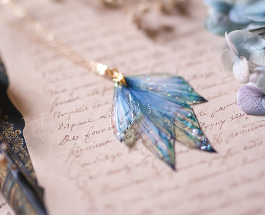 Zoom sur les ailes holographiques du collier Azurelle, révélant des couleurs arc-en-ciel à la lumière, avec détails en strass Swarovski et chaîne en laiton plaqué or.