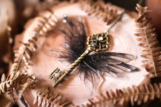 Détails enchanteurs de Ténèbres par Faërie, une clé ailée en bronze noir et violet ornée de paillettes et de strass, parfaite pour sublimer votre tenue nocturne.
