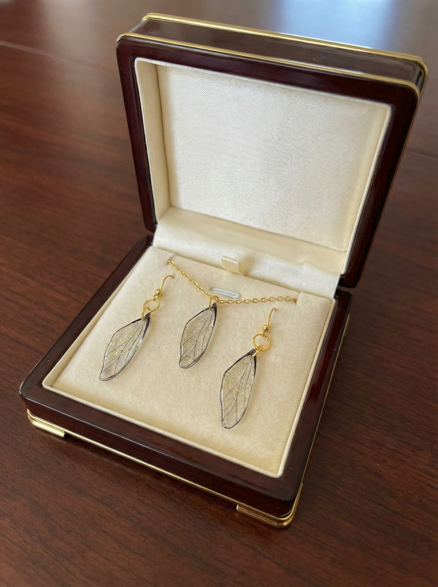 Ensemble collier et paire de boucles d’oreilles - Ailes de Fée Cristallines, d'un design artisanal délicat, en résine translucide et acier inoxydable doré, évoquant la magie et la légèreté des contes de fées.