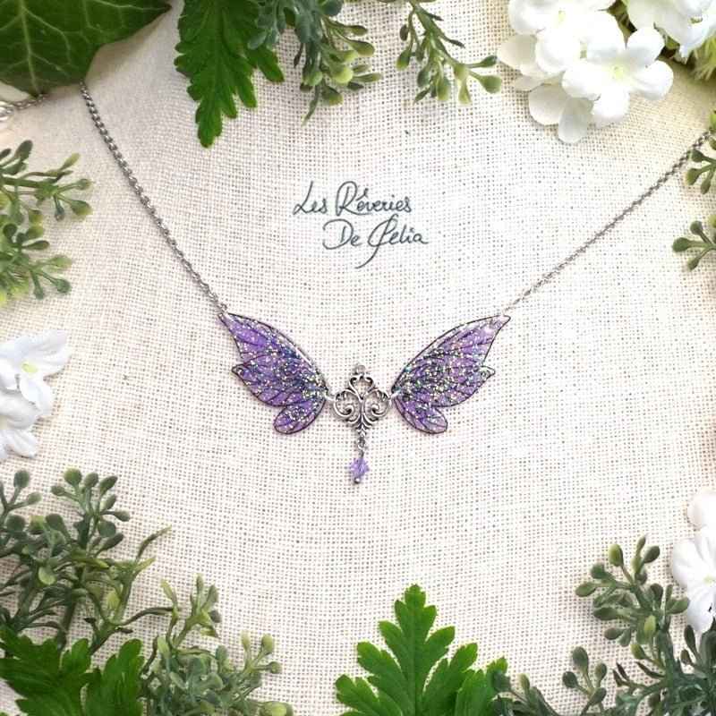 Collier ALDÉRA - Petit collier ailes de fée violet de Les Rêveries de Célia, mettant en valeur des ailes de fée scintillantes et une perle Swarovski élancée, illuminant toute tenue avec une touche de magie.