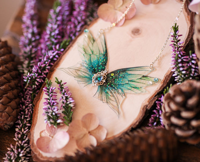 Lac scintillant - Collier orné de quatre Ailes de Fées aux teintes bleu profond et turquoise, décoré de paillettes irisées et d'une pierre bleue centrale, symbolisant la délicatesse et la beauté artisanale.