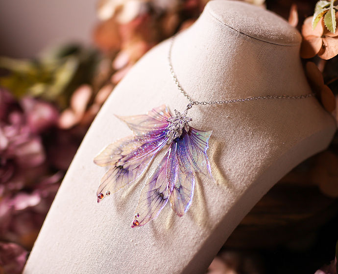 Collier Source aux Fées composé de six Ailes de fée en dégradé violet et bleu, avec paillettes irisées et fleur de verre, parfait pour éblouir sous la lumière.