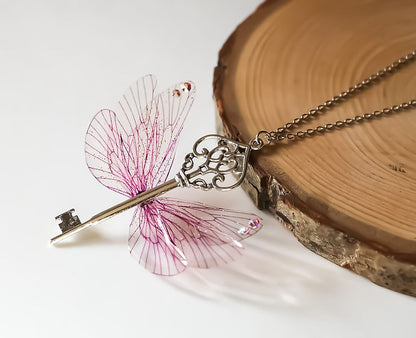 Collier Souffle Féerique en acier chirurgical avec clé centrale délicatement ouvragée et six Ailes de Fées roses, embellies de strass Swarovski.