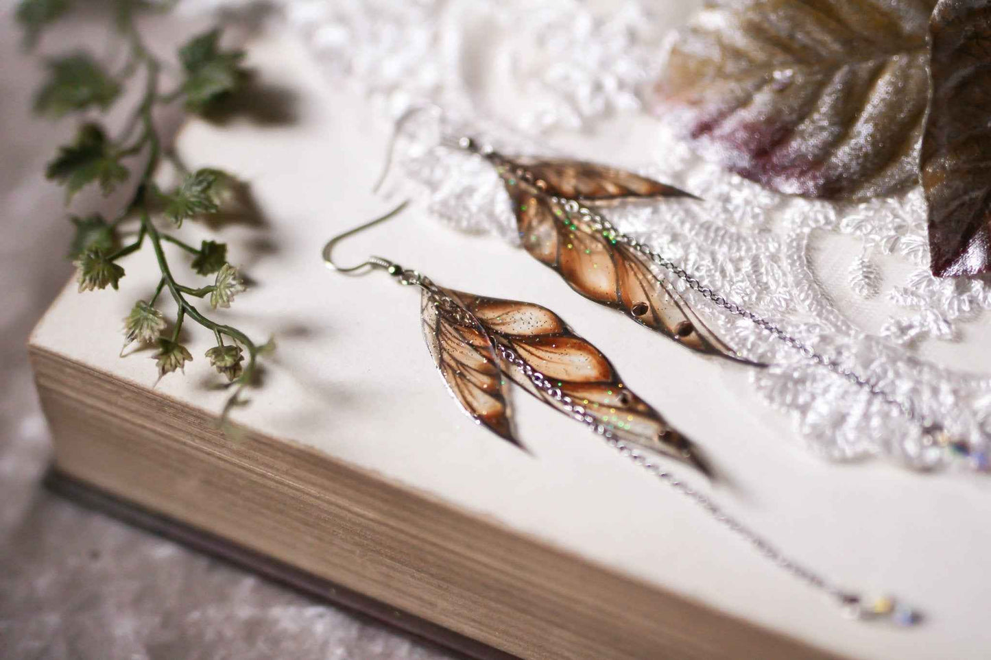 Boucles d'oreilles Conte de Fée par Faërie avec des ailes dorées scintillantes, ornées de paillettes irisées et de strass, parfaites pour illuminer votre style et créer une ambiance magique.