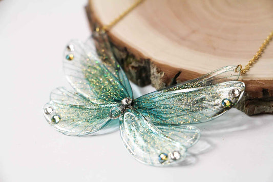 Pendentif Île aux Fées de Faërie, illustrant des Ailes de Fées turquoise ornées de paillettes irisées, ajoutant une touche d'élégance et de magie à chaque look.