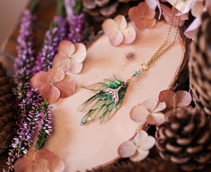 Bijou Luciole Dorée de la marque Faërie, élégant avec des ailes de fée en dégradé bleu et turquoise, parsemées de paillettes scintillantes et orné de perles Swarovski.