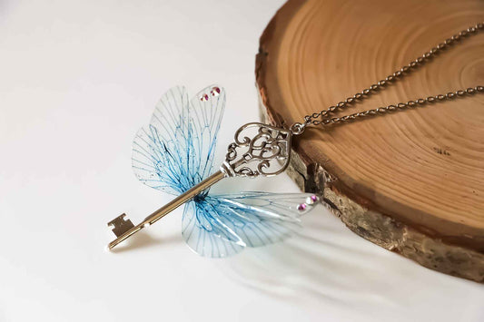 Collier Nuit d’Hiver de Faërie, bijou féérique en acier chirurgical avec clé et Ailes de Fées bleu glacé, parfait pour ajouter une touche d'enchantement à vos tenues.