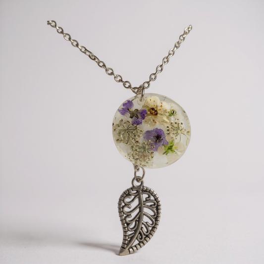 Collier pendentif - Feuille des Jardins Secrets, un bijou artisanal en acier inoxydable avec un médaillon orné de fleurs séchées, qui capture l'élégance de la nature.