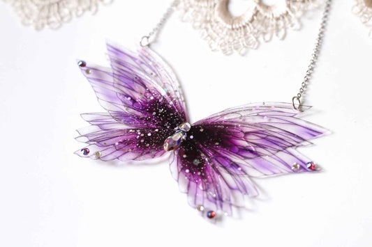 Collier Sauge de Sang de Faërie, orné de cristaux et strass, évoquant la magie et l'élégance avec ses ailes de fées en rouge tendre.