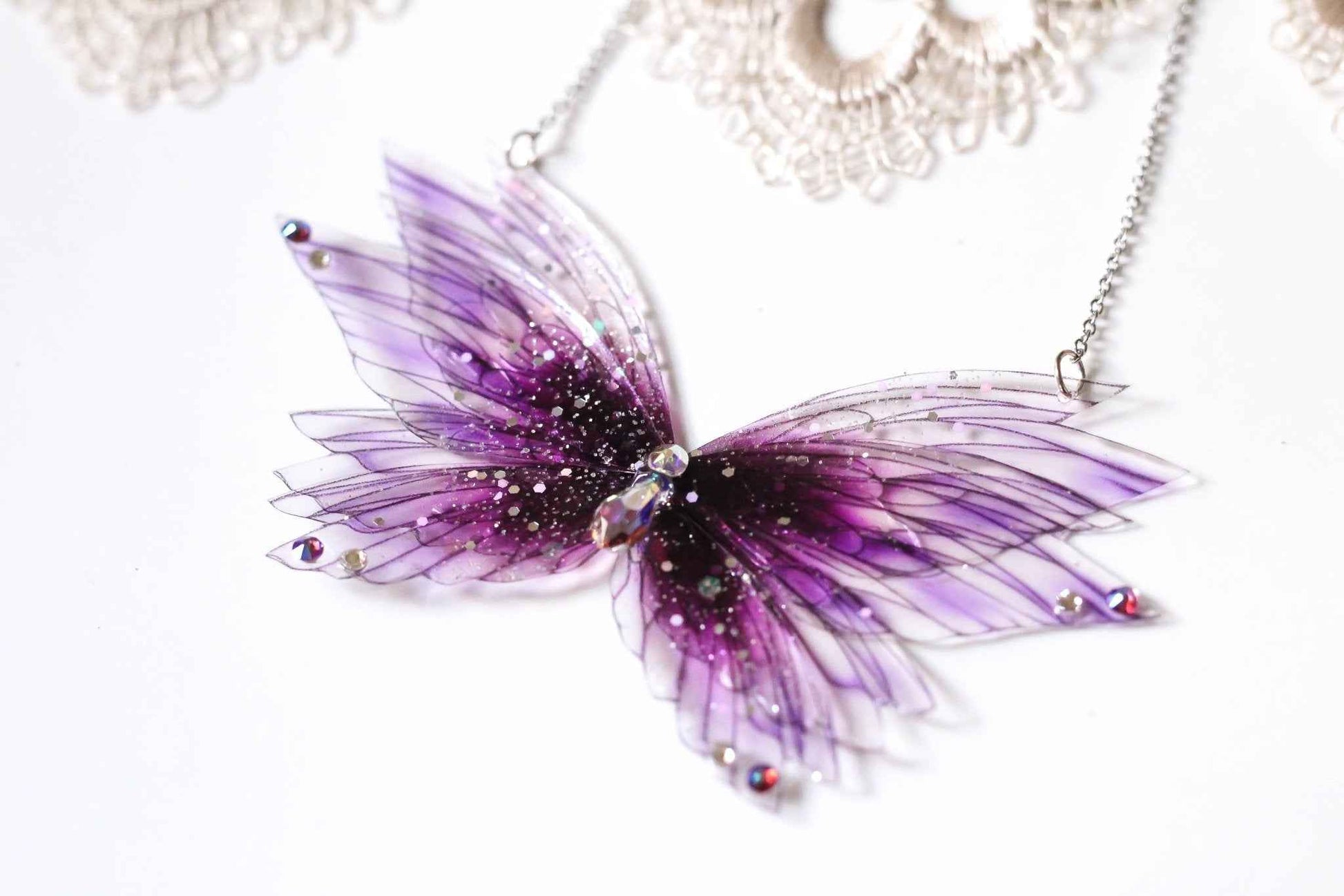 Collier Sauge de Sang de Faërie, orné de cristaux et strass, évoquant la magie et l'élégance avec ses ailes de fées en rouge tendre.