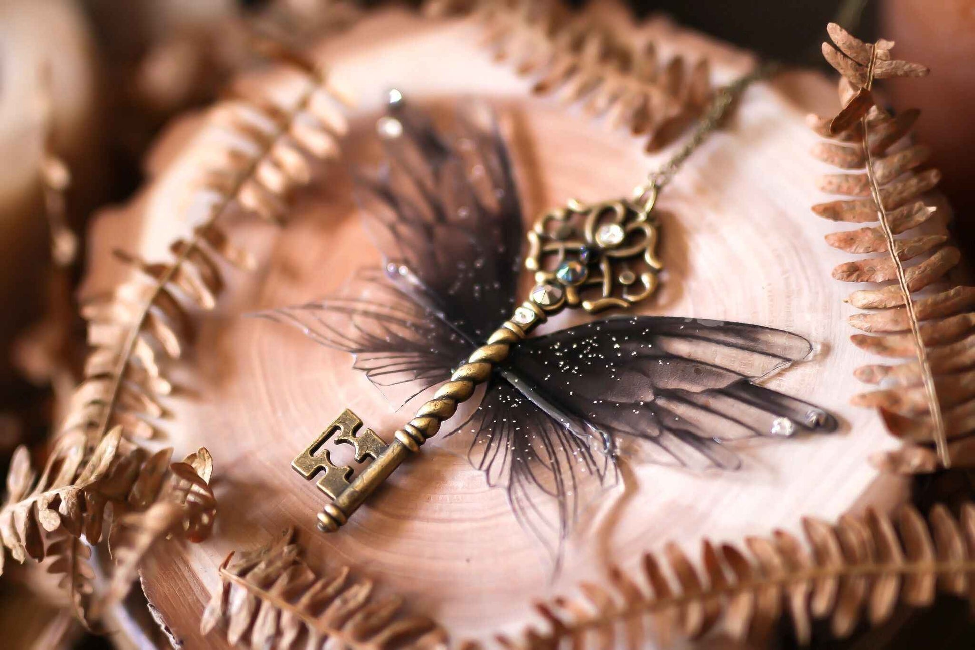 Détails enchanteurs de Ténèbres par Faërie, une clé ailée en bronze noir et violet ornée de paillettes et de strass, parfaite pour sublimer votre tenue nocturne.