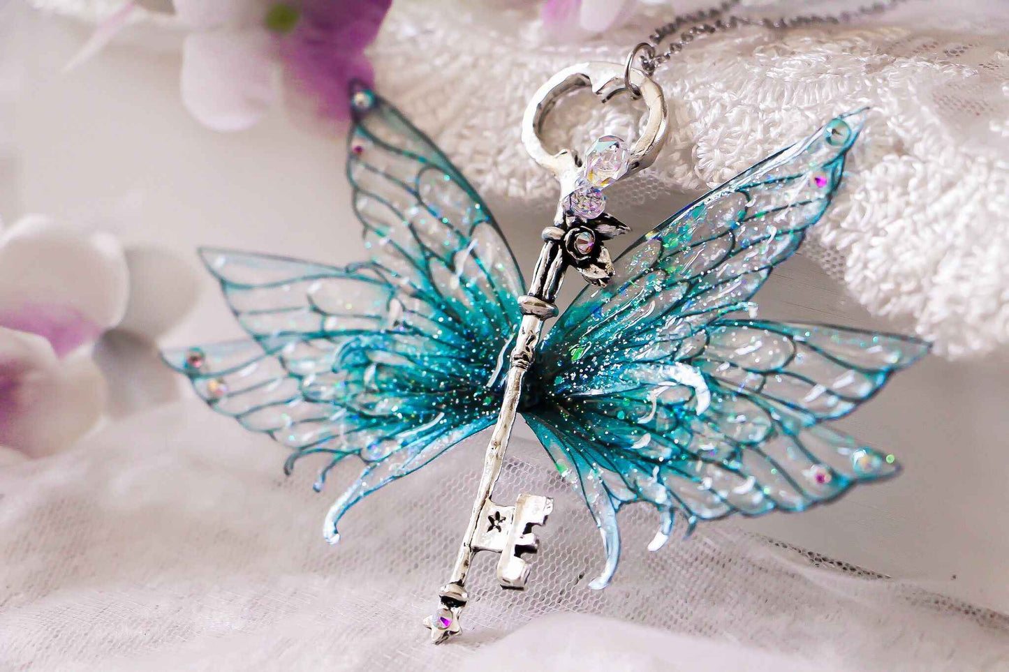 Collier clé-ailée Vague Étincelante de Faërie avec des ailes en bleu turquoise scintillantes, évoquant un monde féerique.